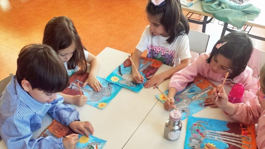 Niños en mesas de colegio realizando una pintura de los elefantes de Dalí