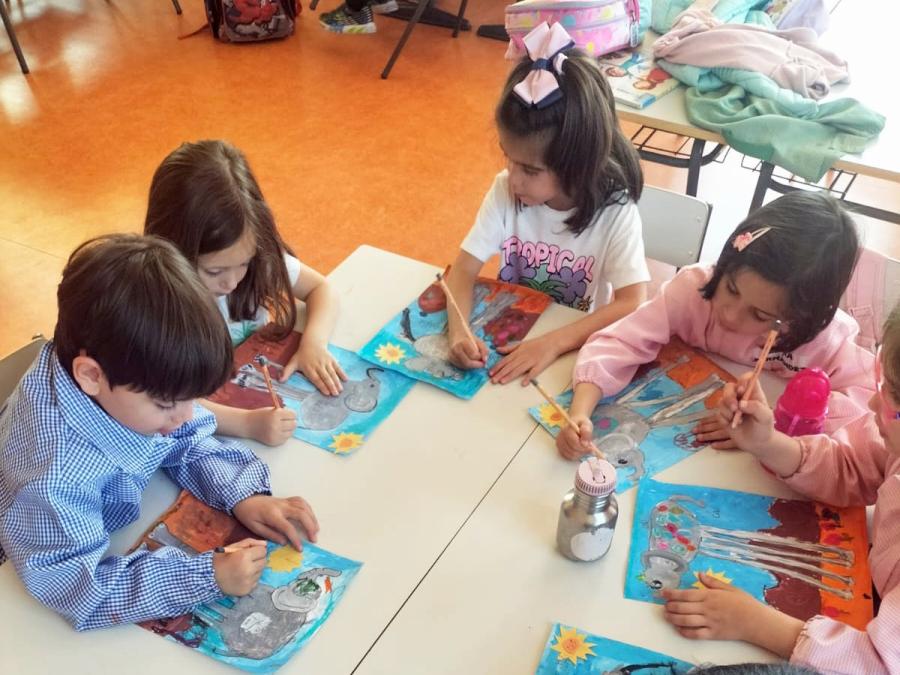 Niños en mesas de colegio realizando una pintura de los elefantes de Dalí